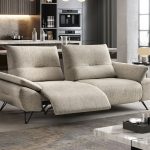 Photo présentant un salon avec un canapé 2 places avec relax. Il y une finition tissu crème gris.