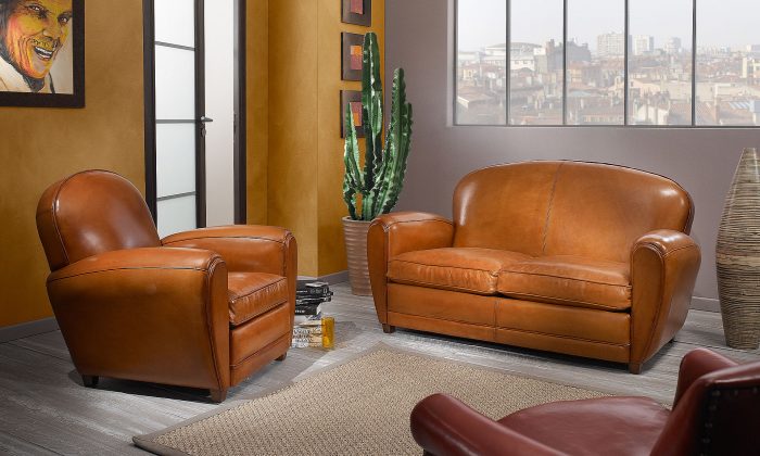 Photo d'un salon avec un canapé et un fauteuil. La finition est cuir et le piétement en bois.